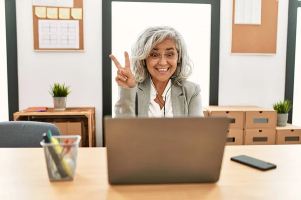 中年女商人坐在办公桌前 在办公室里用笔记本电脑工作 满脸喜色地看着摄像机做胜利标志 第二点 — 图库照片