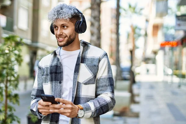 Young hispanic man smiling happy using smartphone and headphones at the city.