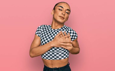 Makyaj yapan, uzun saçlı, modern kıyafetler giyen, göğsünde elleri kapalı, yüzünde minnet ifadesi olan İspanyol transseksüel bir adam. sağlık kavramı. 