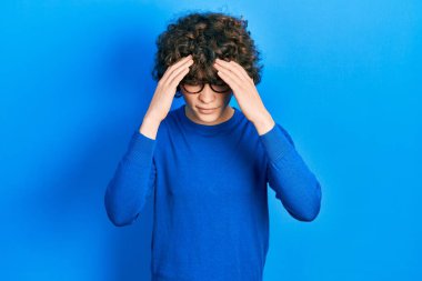 Yakışıklı genç adam, günlük kıyafetler giyiyor ve stres yüzünden başı ağrıyan ellerle gözlük takıyor. migren ağrısı. 