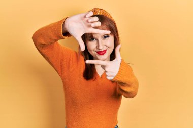 Kızıl saçlı, turuncu süveter giyen, gülümseyen, elleri ve parmakları gülen yüzlü bir kadın. yaratıcılık ve fotoğrafçılık kavramı. 