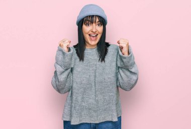 Şirin yün şapkalı genç İspanyol kadın kollarını kaldırıp, gözlerini açarak başarıyı kutluyor ve şaşırıyor. Kazanan konsept. 