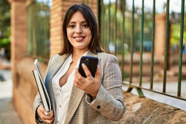 Genç İspanyol iş kadını şehirde akıllı telefon kullanarak mutlu gülümsüyor..