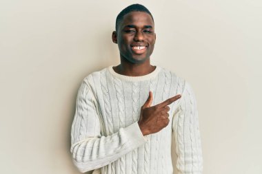 Genç, Afro-Amerikalı, günlük kıyafetler giymiş, neşeli, yüzünde bir gülümsemeyle, mutlu ve doğal bir ifadeyle elini ve parmağını kaldırmış bir adam. 