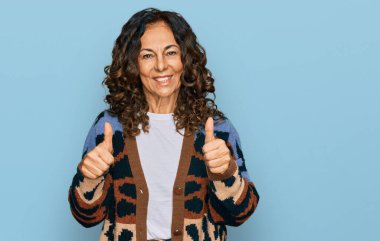 Orta yaşlı İspanyol kadın gündelik kıyafet giyer başarı işareti yapar elle olumlu jest yapar, gülümser ve mutlu olur. Neşeli ifade ve kazanan jest. 