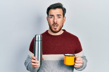 Sakallı yakışıklı beyaz bir adam bir fincan kahve içiyor. Yüzünde termo var. Şüpheci ve alaycı görünüyor. 