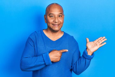 Orta yaşlı, sıradan kıyafetler giyen Latin bir adam kameraya hayret ediyor ve gülümsüyor.. 