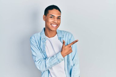 Genç, Afro-Amerikalı, günlük kıyafetler giymiş, neşeli, yüzünde mutlu ve doğal bir ifadeyle, elleri ve parmaklarıyla yüzünü gösteren bir gülümseme var. 