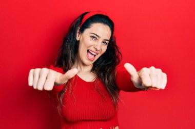 Latin kökenli genç bir kadın, günlük giysiler giyip, olumlu jestler yapıyor, gülümsüyor ve başarı için seviniyor. kazanan jest. 