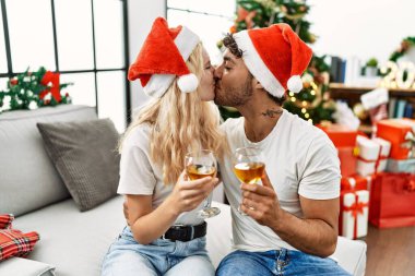 Genç çift Noel şapkası takıyor ve evde şampanyayla kadeh kaldırıyor..