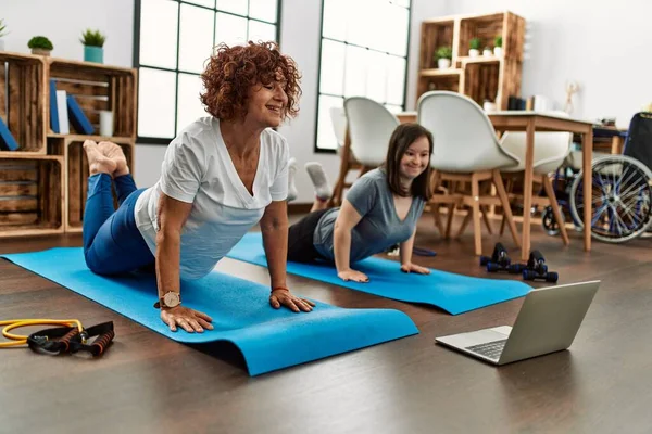 Mature mother and down syndrome daughter doing exercise at home. Stretching at the living room