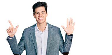 Genç İspanyol adam iş kıyafetleri giyip yedi numaralı parmaklarıyla işaret ederken kendinden emin ve mutlu bir şekilde gülümsüyor.. 