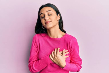 Gündelik kıyafetler giyen genç İspanyol kadın elleri göğsünde, gözleri kapalı ve yüzünde minnet dolu bir jest ile gülümsüyor. sağlık kavramı. 