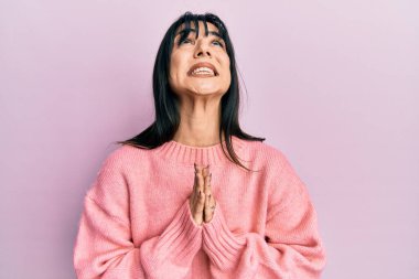 Kâküllü, kışlık süveter giyen genç esmer kadın elleri bağlı yalvarıyor ve dua ediyor. Yüzünde umut ifadesi var. Çok duygusal ve endişeli. Yalvarıyor. 