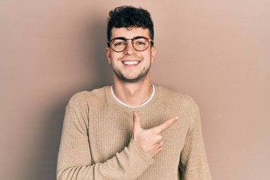 Genç İspanyol bir adam günlük kıyafetler ve gözlük takıyor. Neşeli, yüzünde bir gülümseme var. Yüzünde mutlu ve doğal bir ifade var. 