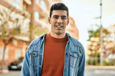 Genç İspanyol adam gülümseyerek şehirde mutlu mesut dikiliyor..