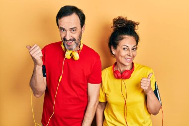 Orta yaşlı bir çift İspanyol kadın ve erkek spor giysisi ve kol bandı takıyor. Gülümsüyor, gülümsüyor ve başparmağıyla yana bakıyor.. 