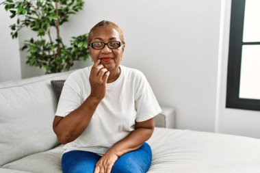 Evde kanepede oturan olgun İspanyol kadın elleri ağzında çivi yerken gergin ve stresli görünüyor. anksiyete. 