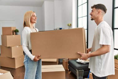 Genç beyaz çift mutlu bir şekilde gülümsüyor. Yeni evlerinde karton kutular tutuyorlar..