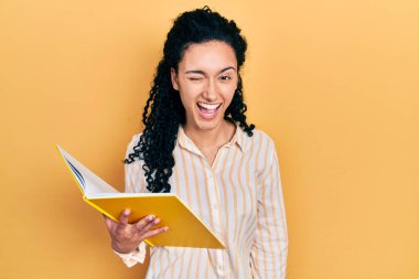 Kıvırcık saçlı, kitap okuyan genç İspanyol kadın kameraya seksi bir ifadeyle bakıyor, neşeli ve mutlu bir yüzle.. 