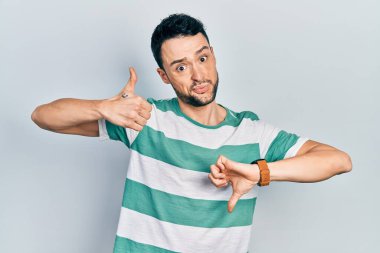 Latin asıllı genç bir adam günlük kıyafetler giyip baş parmak kaldırıyor, anlaşmazlık ve uzlaşma ifadesi. çılgın çatışma 