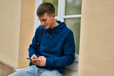 Üniversitede akıllı telefon kullanarak mutlu gülümseyen genç sarışın öğrenci..