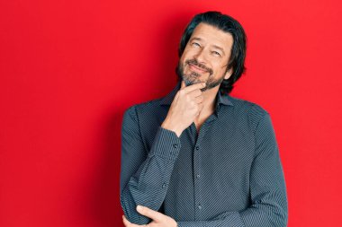 Orta yaşlı, günlük kıyafetler giyen, kameraya kendinden emin, kolları çapraz ve çenesi havada gülümseyen beyaz bir adam. Olumlu düşünmek. 