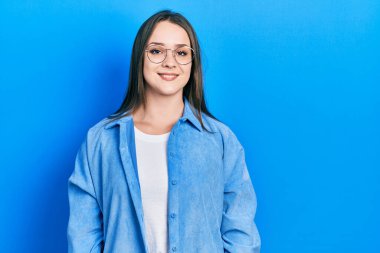 Gündelik kıyafetler ve gözlük takan genç İspanyol kız pozitif ve mutlu görünüyor ve kendine güvenen bir gülümsemeyle dişlerini gösteriyor. 