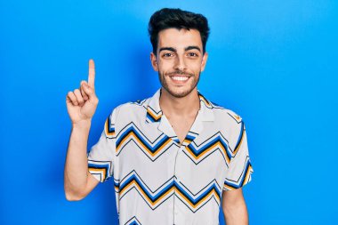 Gündelik kıyafetler giyen genç İspanyol bir numarayı gösterip işaret ederken kendinden emin ve mutlu bir şekilde gülümsüyor.. 