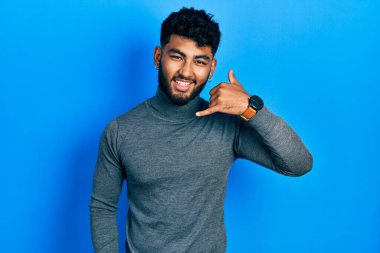 Balıkçı yaka kazak giyen, gülümseyen, el ve parmaklarıyla telefonla konuşan Arap bir adam. iletişim kavramları. 