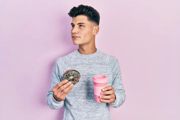 Jovem Hispânico Comendo Donut Bebendo Café Sorrindo Olhando Para Lado — Fotografia de Stock