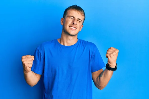 年轻的高加索人穿着休闲的蓝色T恤 非常高兴而兴奋地举起双臂做着获胜的手势 微笑着 尖叫着要成功 庆祝概念 — 图库照片