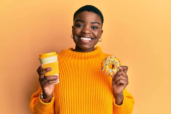 若いアフリカ系アメリカ人女性がドーナツを食べ コーヒーを飲みながら笑顔でコーヒーを飲みます 歯を見せて — ストック写真