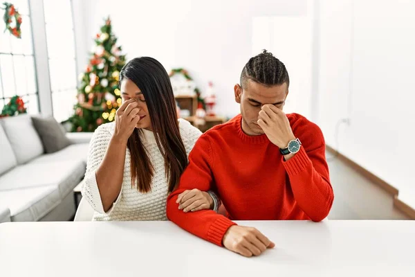 Young Latin Couple Sitting Table Christmas Tree Tired Rubbing Nose — Fotografia de Stock
