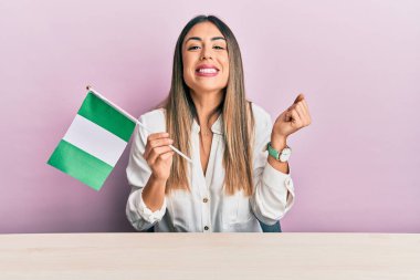 Genç İspanyol kadın elinde Nijerya bayrağı, masaya oturmuş gururla bağırıyor zaferi ve başarıyı kutluyor. 