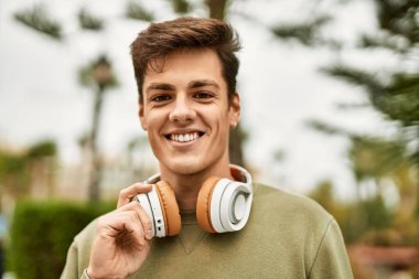 Şehirde kulaklık takarak mutlu gülümseyen genç İspanyol adam..