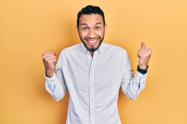 Sakallı, iş gömleği giyen İspanyol adam kollarını kaldırıp gözleri açık bir şekilde başarıyı kutluyor ve şaşırıyor. Kazanan konsept. 