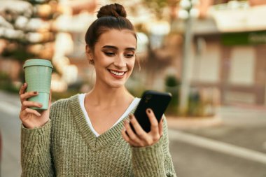 Güzel esmer kadın mutlu ve kendinden emin bir şekilde gülümsüyor. Güneşli bir sonbahar gününde akıllı telefon kullanıyor.