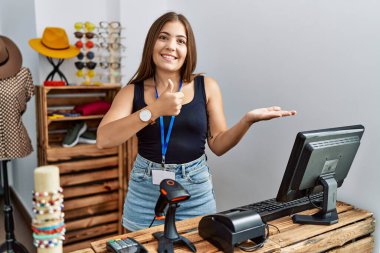 Perakende dükkanında açık mesajla pankart tutan genç esmer kadın avuç içini gösteriyor ve baş parmaklarıyla hareket ediyor, mutlu ve neşeli gülümsüyor. 