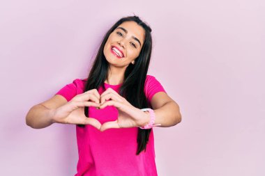 Sevgiyle gülümseyen, sıradan pembe tişörtler giyen genç İspanyol kız elleriyle kalp sembolü yapıyor. romantik kavram. 