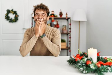 Masada sakallı genç yakışıklı adam Noel süslemeleri ile oturuyor gülüyor ve utanıyor kıkırdıyor ağızları ellerle, dedikodularla ve skandallarla örtüyor. 