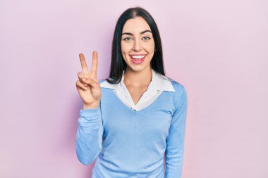 Pembe arka planda duran mavi gözlü güzel kadın iki numaralı parmaklarıyla işaret ederken kendinden emin ve mutlu bir şekilde gülümsüyor.. 