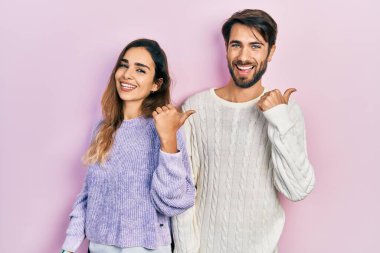 Mutlu yüzlü gülümseyen gündelik kıyafetler giyen genç İspanyol çift başparmağıyla yana bakıyor ve işaret ediyor.. 