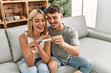 Genç beyaz çift mutlu bir şekilde gülümsüyor. Evde hamilelik testi yapıyorlar..