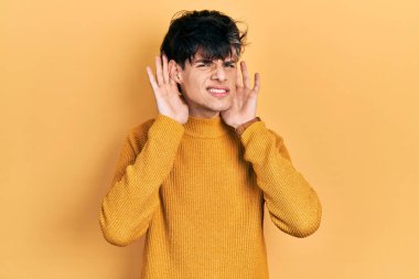 Yakışıklı hippi genç adam gündelik sarı süveter giyiyor iki elini de kulak hareketi yaparken duymaya çalışıyor, dedikoduya meraklı. İşitme sorunu, sağır 