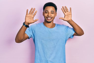 Genç Afro-Amerikan adam günlük mavi tişört giyer ve parmaklarıyla on numarayı gösterirken kendinden emin ve mutlu gülümserdi.. 