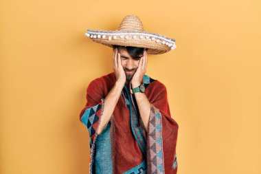 Meksikalı şapkalı genç İspanyol adam acı ve migren yüzünden çaresiz ve stresli bir şekilde baş ağrısı çekiyor. Eller başının üstünde.. 