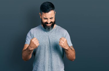 Günlük gri tişörtlü İspanyol adam kolları havada ve gözleri kapalı bir şekilde başarıyı kutluyor ve şaşırıyor. 