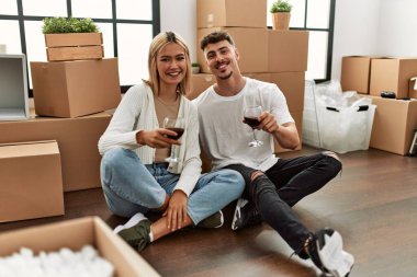 Kırmızı şarap kadehleriyle kadeh kaldıran beyaz bir çift yeni evlerinde oturuyor..