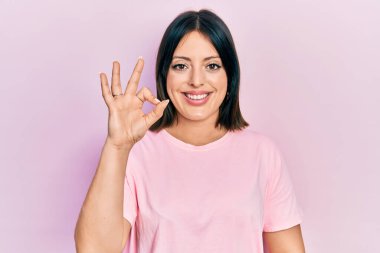 Günlük pembe tişört giyen genç İspanyol kadın gülümsüyor ve el ve parmaklarıyla 